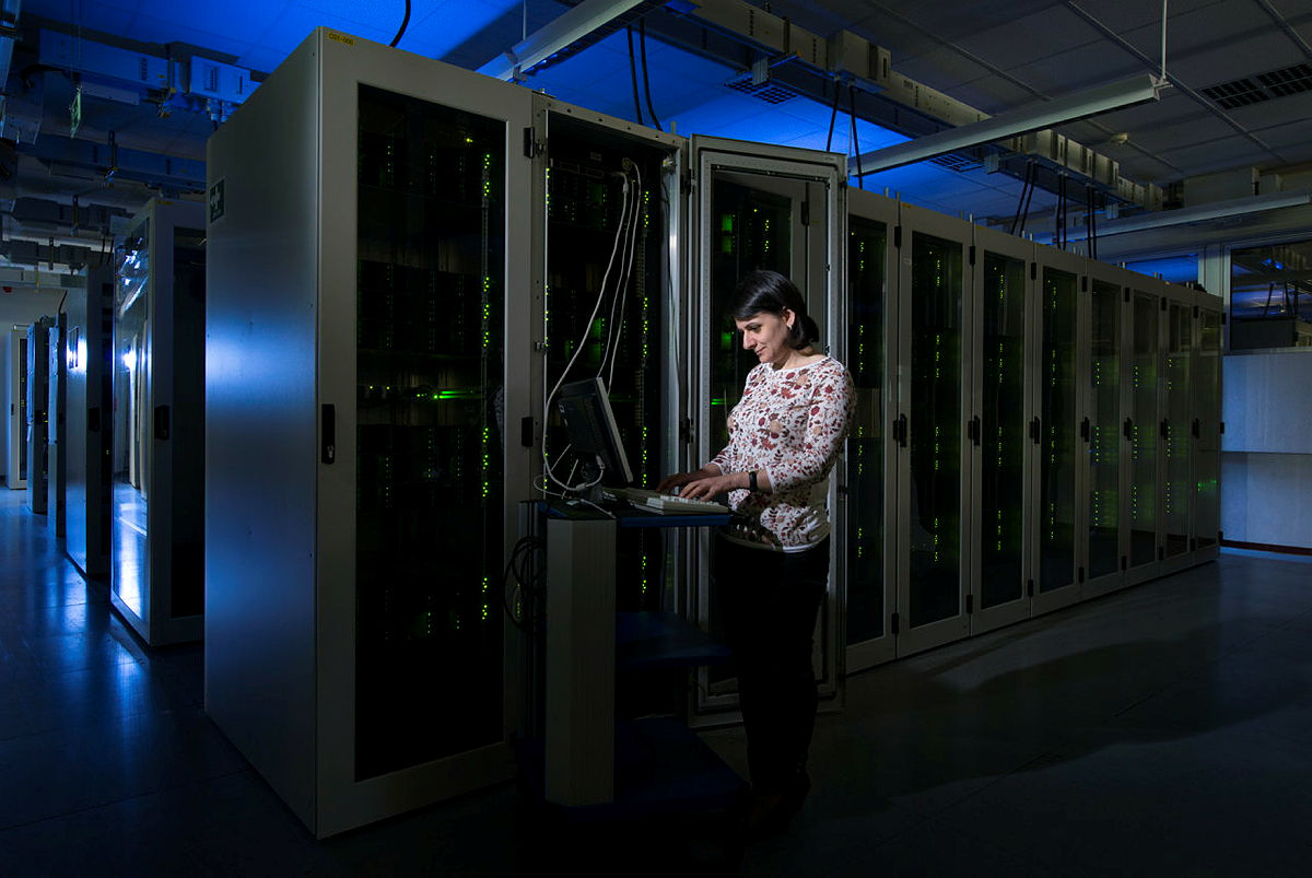 Blick in das Grid Computing Centre Karlsruhe mit seinen hunderten von Rechnerschränken, Eine Person steht an einer Laptop-Konsole und startet neue Maschinen.