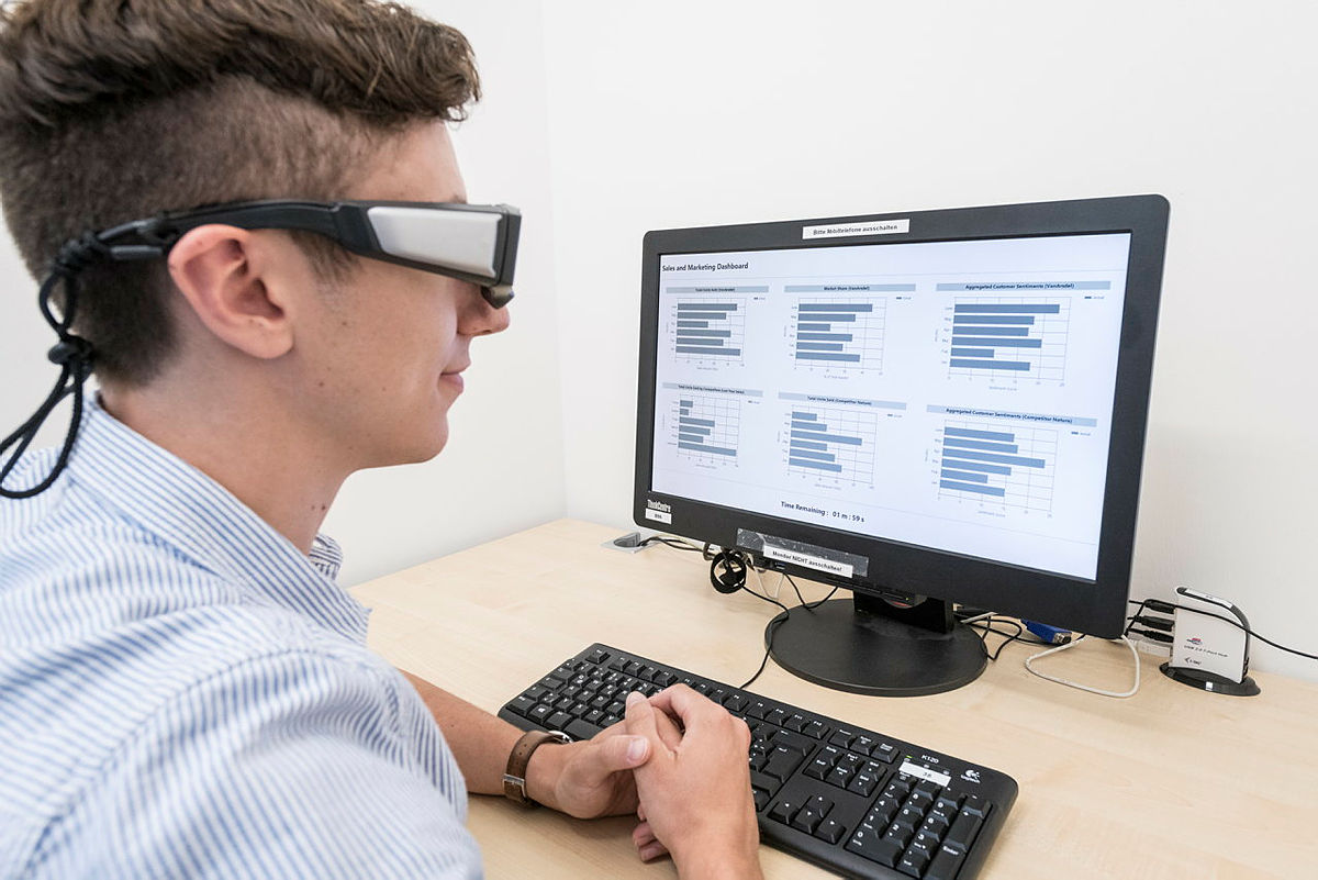 Eine Person sitzt mit einer Virtual Reality Brille an einem Bildschirm und sichtet Diagramme