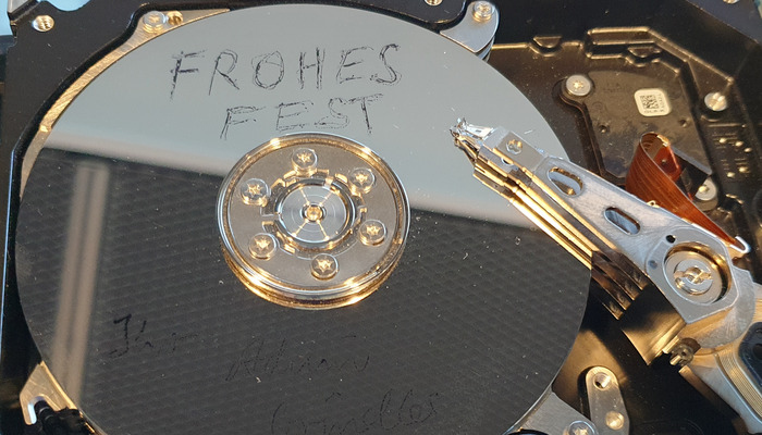 Foto zeigt eine geöffnete Harddisk, deren spiegelnde Oberfläche sich im neuen Serverraum lila "einkleidet". Oben auf der Platte steht "Frohes Fest"  (c) Achim Grindler 